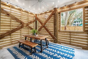 A room with a wooden slatted wall, a ceiling fan, a table with a bench, and a patterned rug.