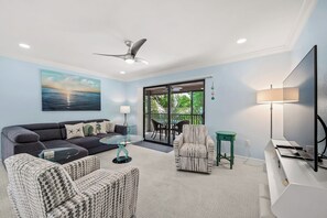 Ein Wohnzimmer mit einer Couch, Sesseln, einem Couchtisch, einem Fernseher und einem Balkon mit Blick.