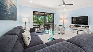 A living room with a sofa, a glass coffee table, a TV, and a ceiling fan. - Cozy Dockside 2 bed, 2 bath at Sanibel Moorings #1422 (Sanibel)