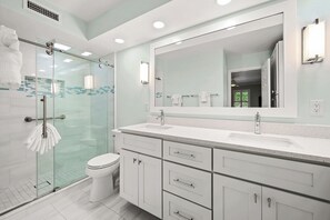 Une salle de bain moderne avec une douche à parois de verre, des toilettes blanches, un grand miroir et un plan de toilette avec un lavabo.