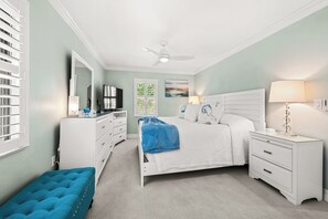 Ein Schlafzimmer mit Bett, Kommode, Fernseher, Deckenventilator und einem Fenster mit Jalousien.