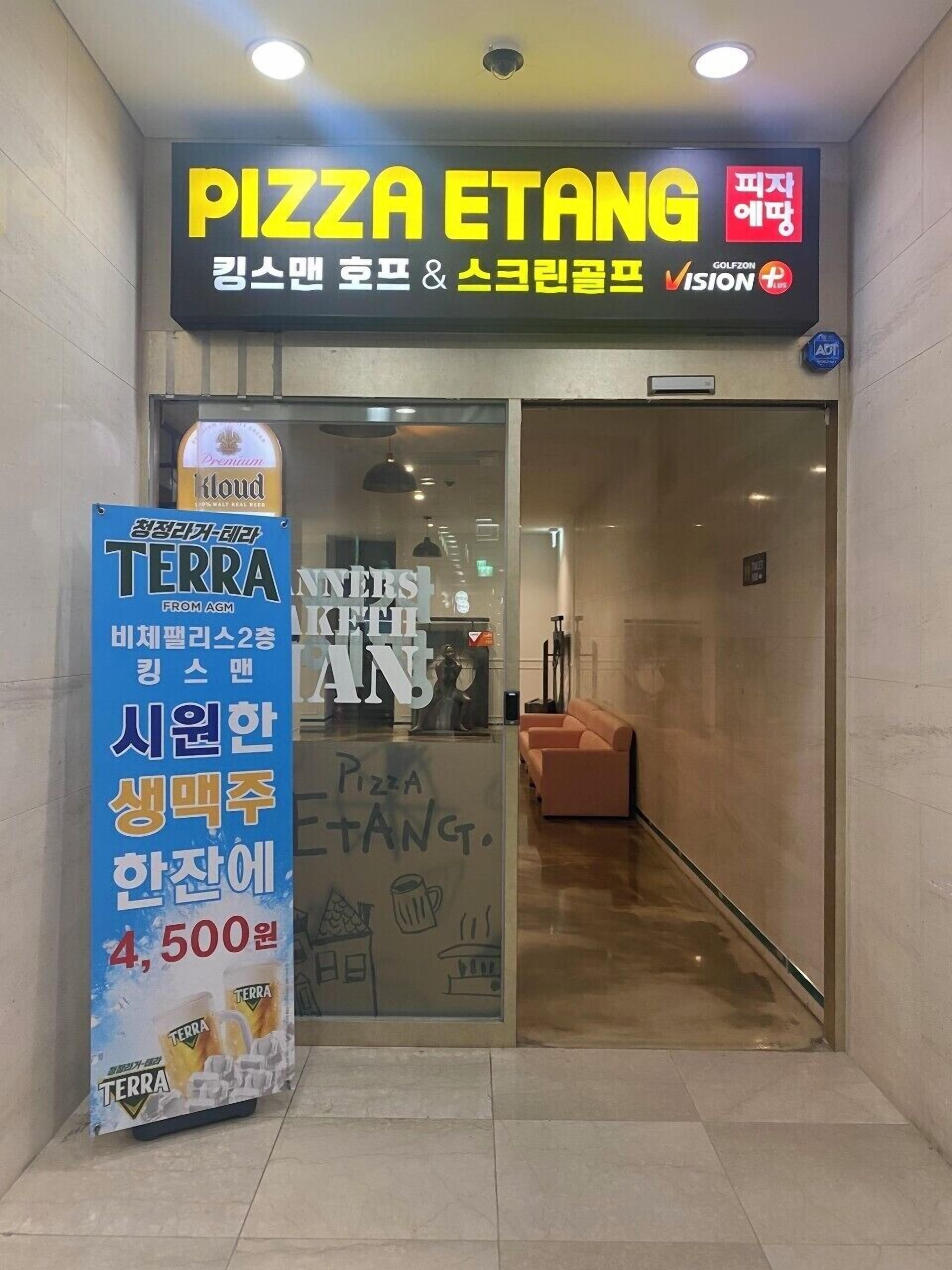 La entrada a una pizzería llamada PIZZA ETANG, con un cartel con texto coreano y un anuncio de cerveza TERRA.