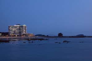 Ein Hochhaus-Hotel mit mehreren Etagen und Balkonen, gelegen in Strandnähe mit Felsen und ruhigem Wasser.