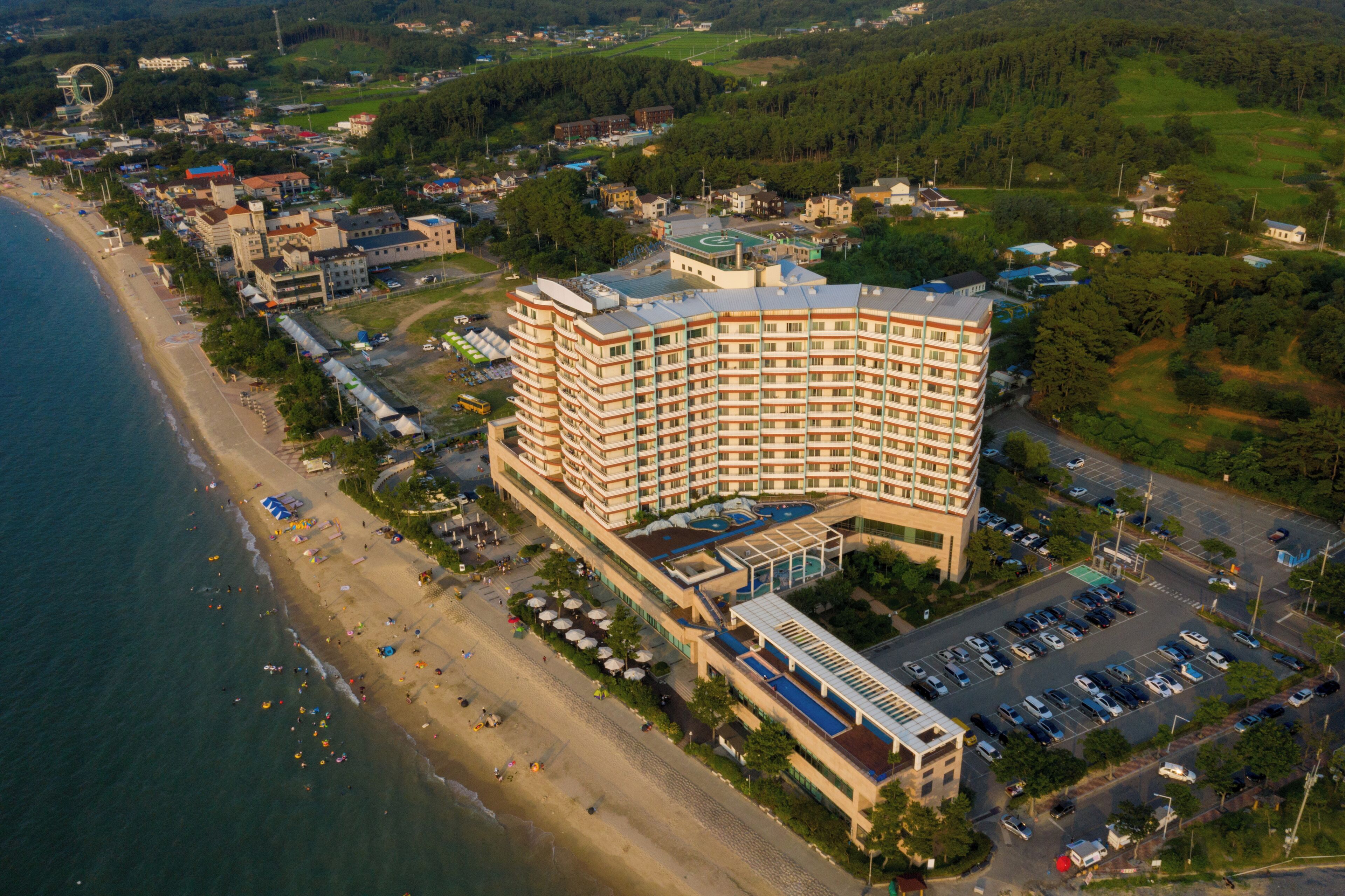 Vista aérea de un hotel costero con amplio estacionamiento, acceso directo a la playa y un edificio central de varios pisos.