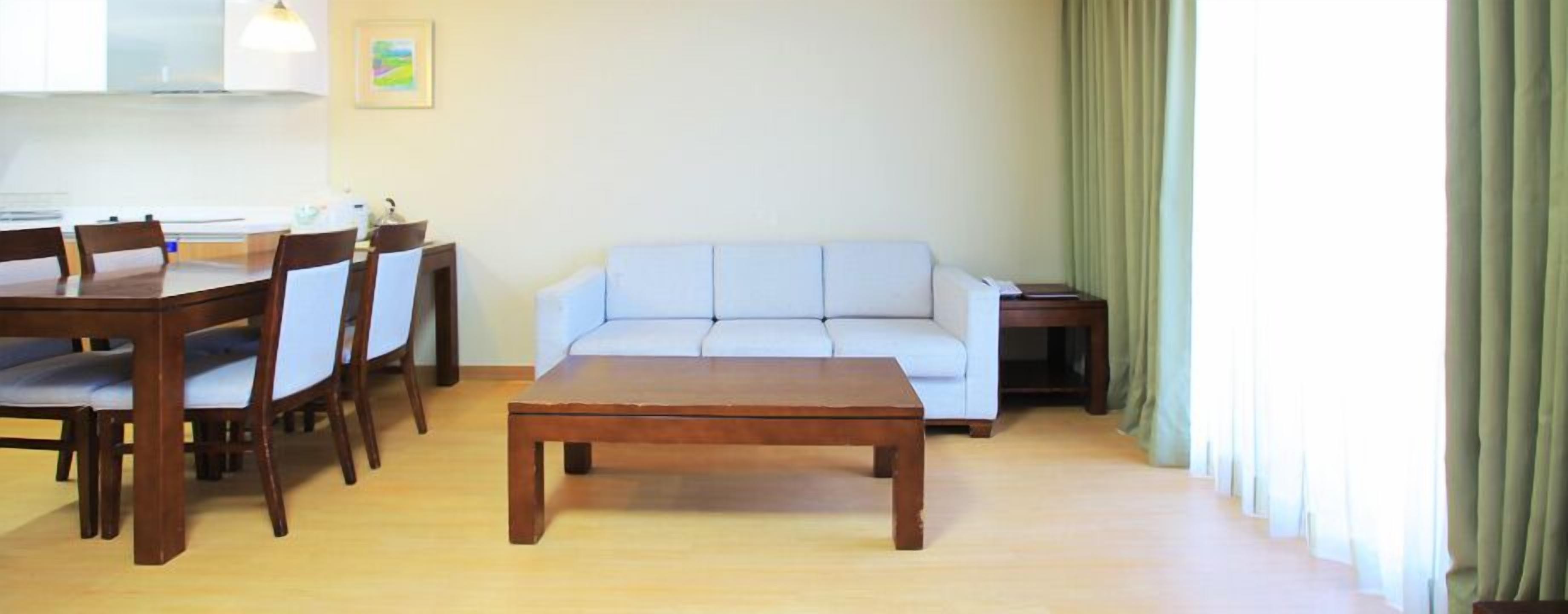A living room with a wooden coffee table, a white sofa, and a dining table with chairs.