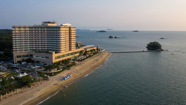 A high-rise hotel with multiple floors, a beach in the foreground, and a calm sea with distant islands. - Beache Palace (Boryeong)