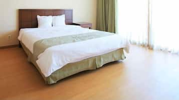 A hotel room with a wooden floor, a bed with a headboard, a bedside table, and a window with curtains.