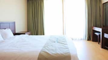 Une chambre d’hôtel avec un lit, une table de chevet, un bureau et une fenêtre avec des rideaux.