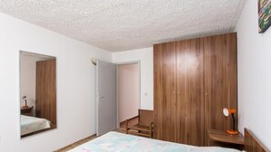 Une chambre à coucher comprenant un lit, une armoire, un miroir et un bureau avec une lampe.