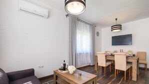 Un soggiorno moderno con divano, tavolino in legno e zona pranzo con tavolo e sedie. C'è una TV a schermo piatto montata a parete e un condizionatore d'aria.