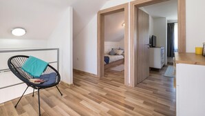 Una camera moderna e luminosa, con pavimento in legno, una sedia nera con cuscino verde acqua, un letto con copripiumino blu e bianco e una piccola scrivania con un televisore.