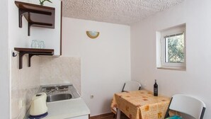 Eine kompakte Küche mit Gasherd, Spüle und einem kleinen Tisch mit Tischdecke. Ein Fenster bietet Blick ins Grüne.
