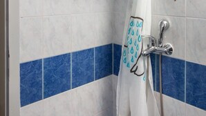 Ein Duschbereich mit blauen und weißen Fliesen, einem weißen Duschvorhang und einer Handbrause.