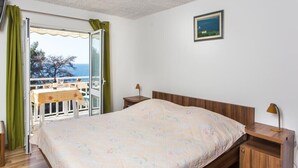 Ein Schlafzimmer mit einem Bett, einem Nachttisch, einem Tisch mit Stuhl und Meerblick durch eine Glastür.