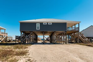 A two-story building with a balcony on the upper floor, a wooden deck, and a sandy ground area.