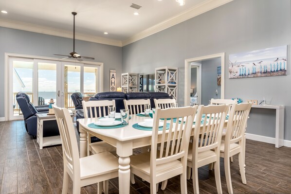 A dining area with a white table and chairs, a ceiling fan, and a view through glass doors to the outside.