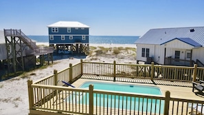 A beach house with a pool, wooden deck, and a view of the ocean.