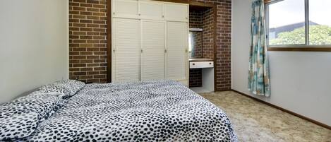 A bedroom with a brick wall, a bed with a leopard print bedspread, a white wardrobe, and a window with curtains.