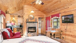 Una acogedora habitación tipo cabaña de madera con chimenea, un comedor y un televisor montado en la pared.
