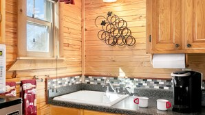 Una cocina compacta con armarios de madera, encimera de granito, pileta blanca y cafetera.