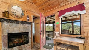 Un interior acogedor de cabaña con chimenea de piedra, paredes de madera, zona de comedor y un ventanal con vistas al exterior.