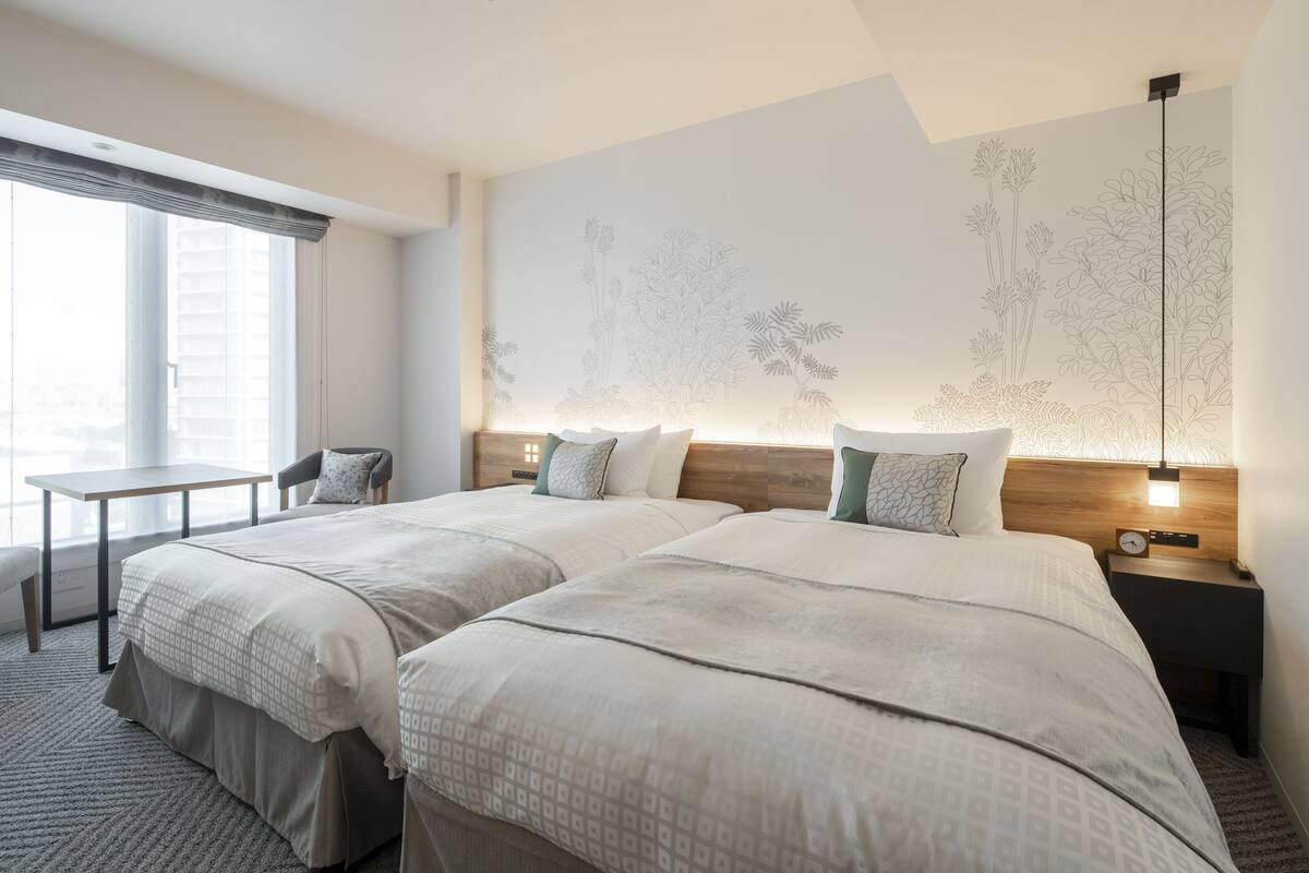 A hotel room with two beds, a small table, and a nightstand with a clock.