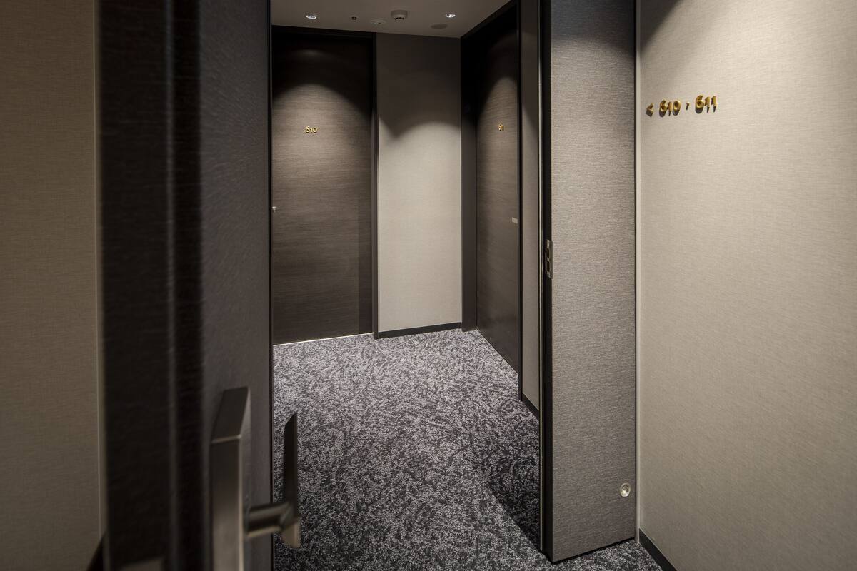 A narrow hallway with a carpeted floor, a door with a metallic handle, and a wall with a number sign.