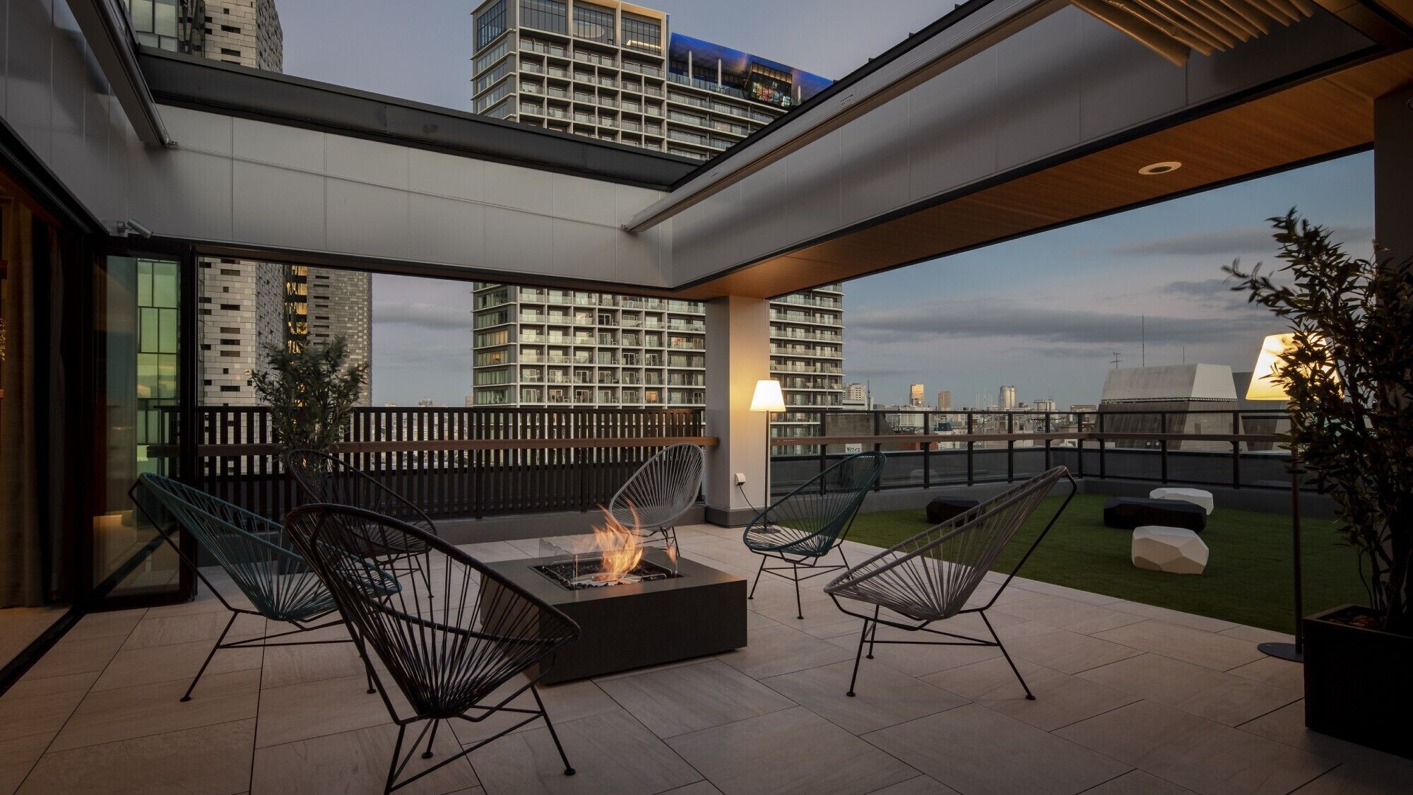 A rooftop terrace with a fire pit, outdoor seating, and a view of the city skyline.