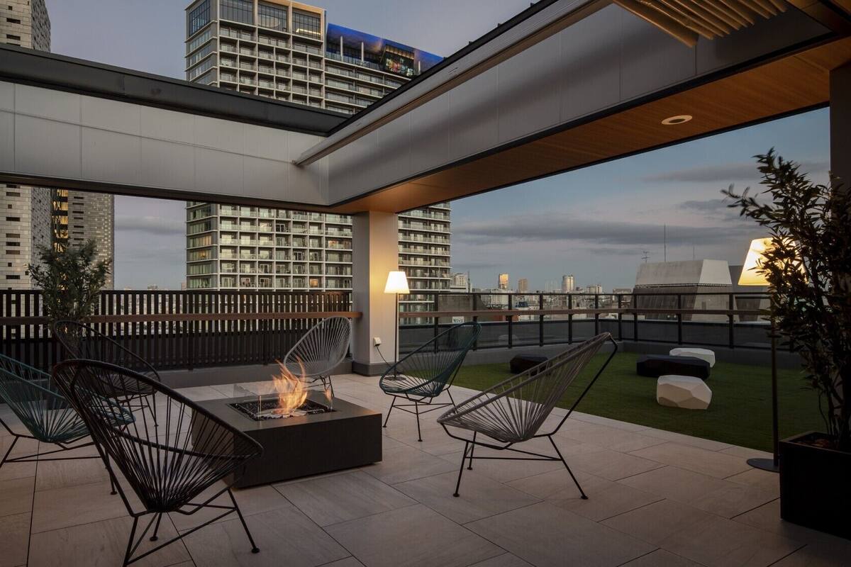A rooftop terrace with a fire pit, outdoor seating, and a view of the city skyline.