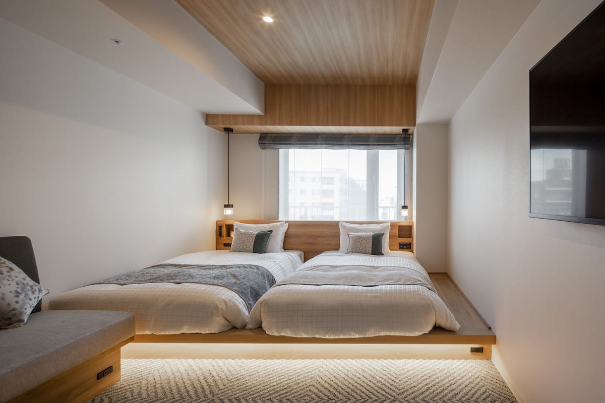 A modern bedroom with a loft bed, a bedside table, and a built-in TV.