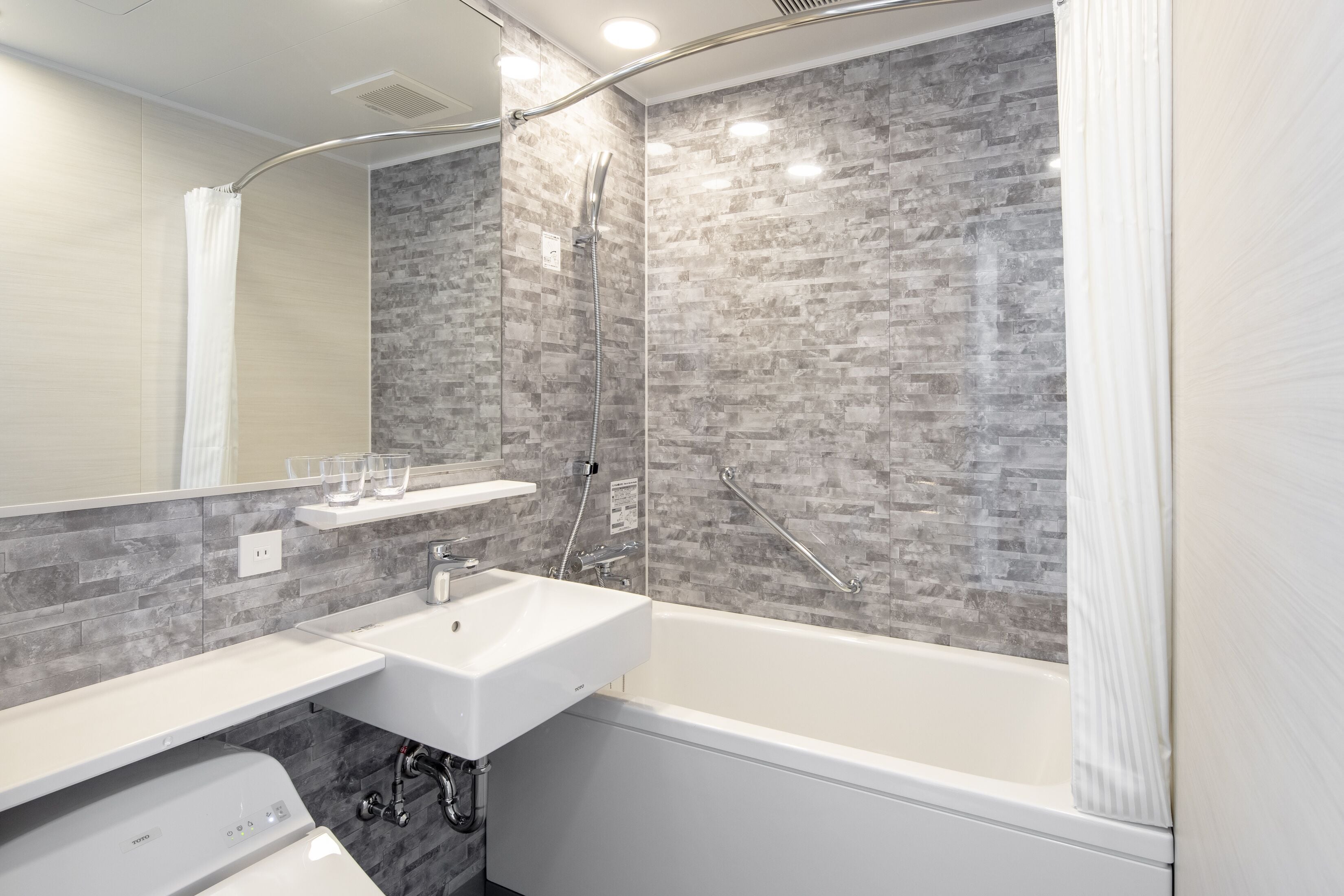 Une salle de bain moderne avec une baignoire blanche, un lavabo blanc et une douche dotée d’une porte en verre.