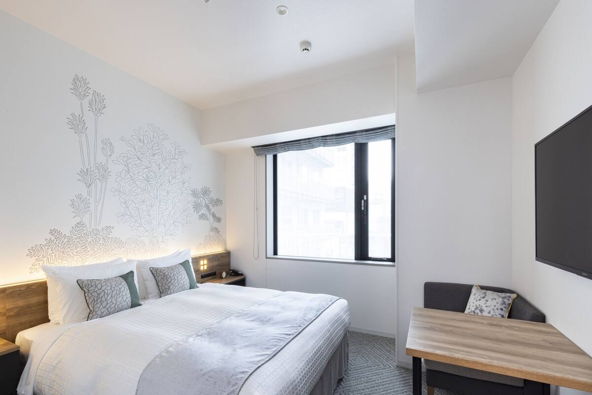A modern hotel room with a large bed, a desk, and a large window.