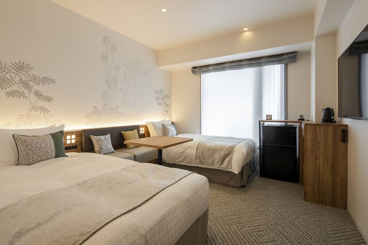 A hotel room with two beds, a small table, a TV, and a refrigerator.