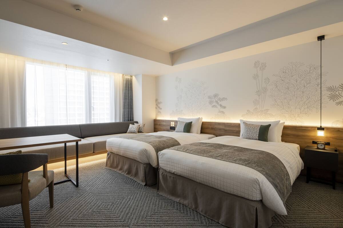 A hotel room with two beds, a sofa, a desk, and a large window with curtains.