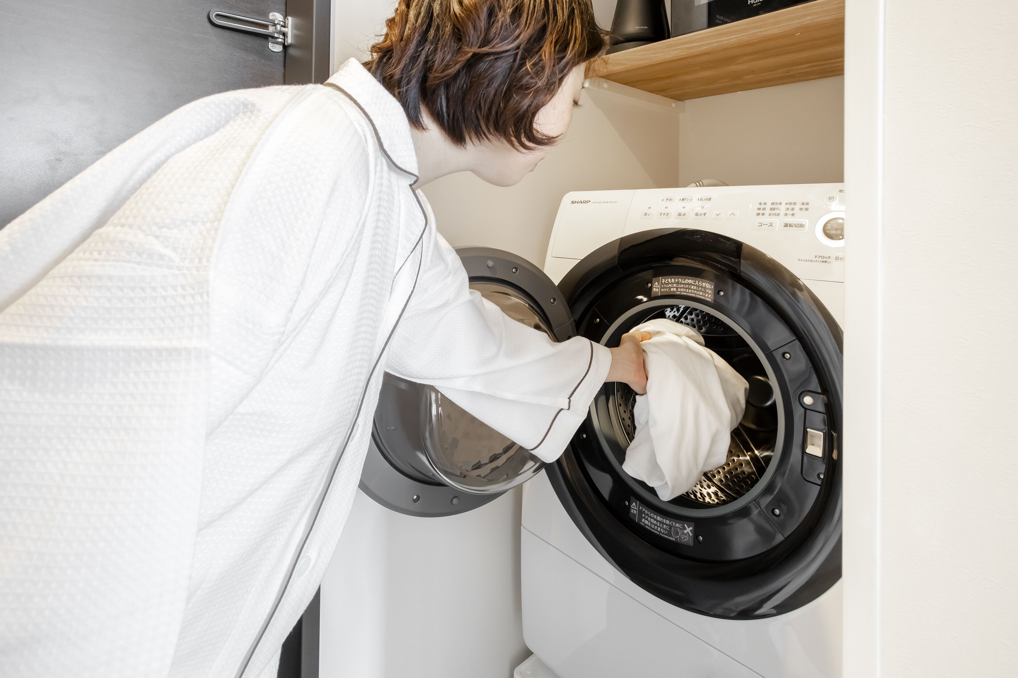 A person loading a white towel into a front-loading washing machine.