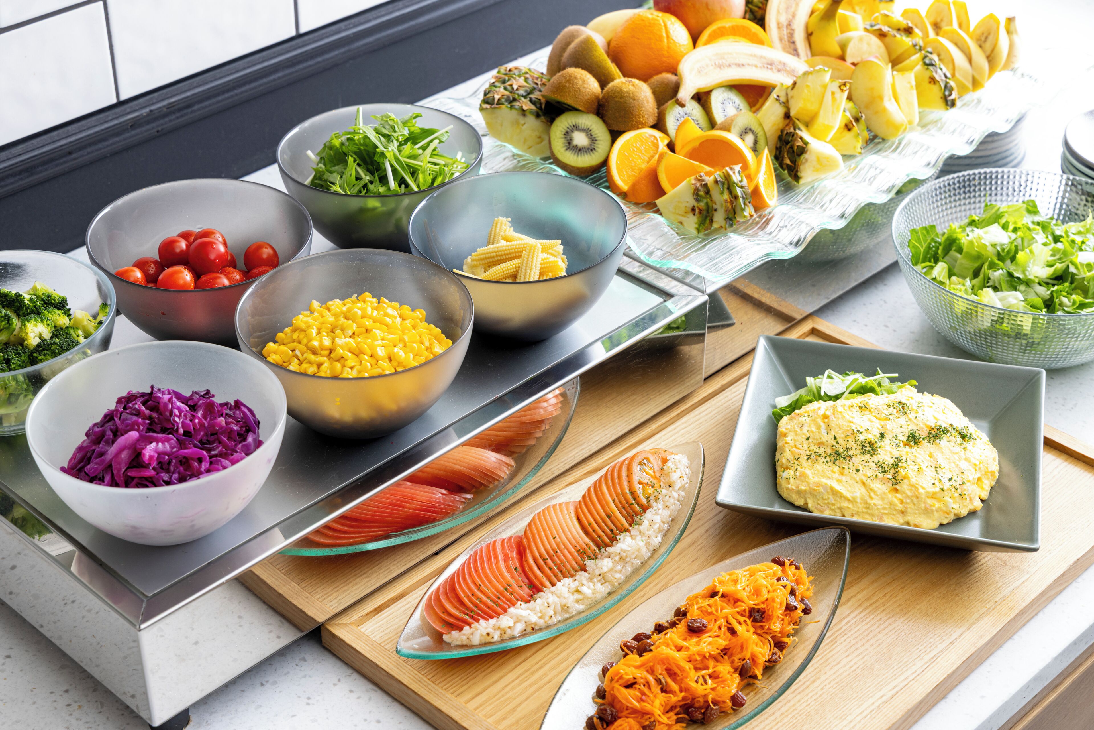 A variety of food items displayed on a kitchen counter, including bowls of vegetables, fruits, and a plate of salmon.