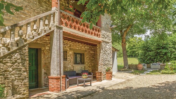 Un edificio de piedra con un porche cubierto, mobiliario exterior y un camino de grava.