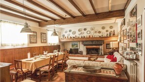 Comedor tradicional con vigas de madera, chimenea y una pared decorada con platos y fotos enmarcadas.