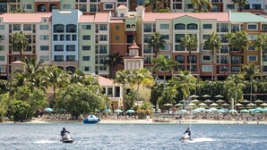 A beachfront hotel with multiple stories, palm trees, and beach umbrellas.