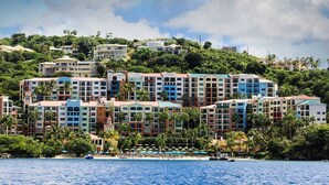 A multi-story hotel with balconies, located on a hillside overlooking a beach.