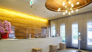A reception area with a wooden wall, a vase of flowers, a reception desk, and a modern chandelier. - Far East Village Hotel Yokohama (Yokohama)