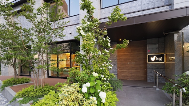 A hotel entrance with a modern facade, a well-maintained garden with various plants, and a clear view of the hotel's name on the sign. - Far East Village Hotel Yokohama (Yokohama)