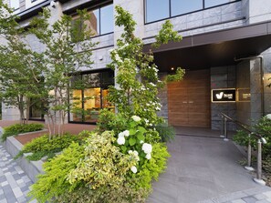 A hotel entrance with a modern facade, a well-maintained garden with various plants, and a clear view of the hotel's name on the sign. - Far East Village Hotel Yokohama (Yokohama)