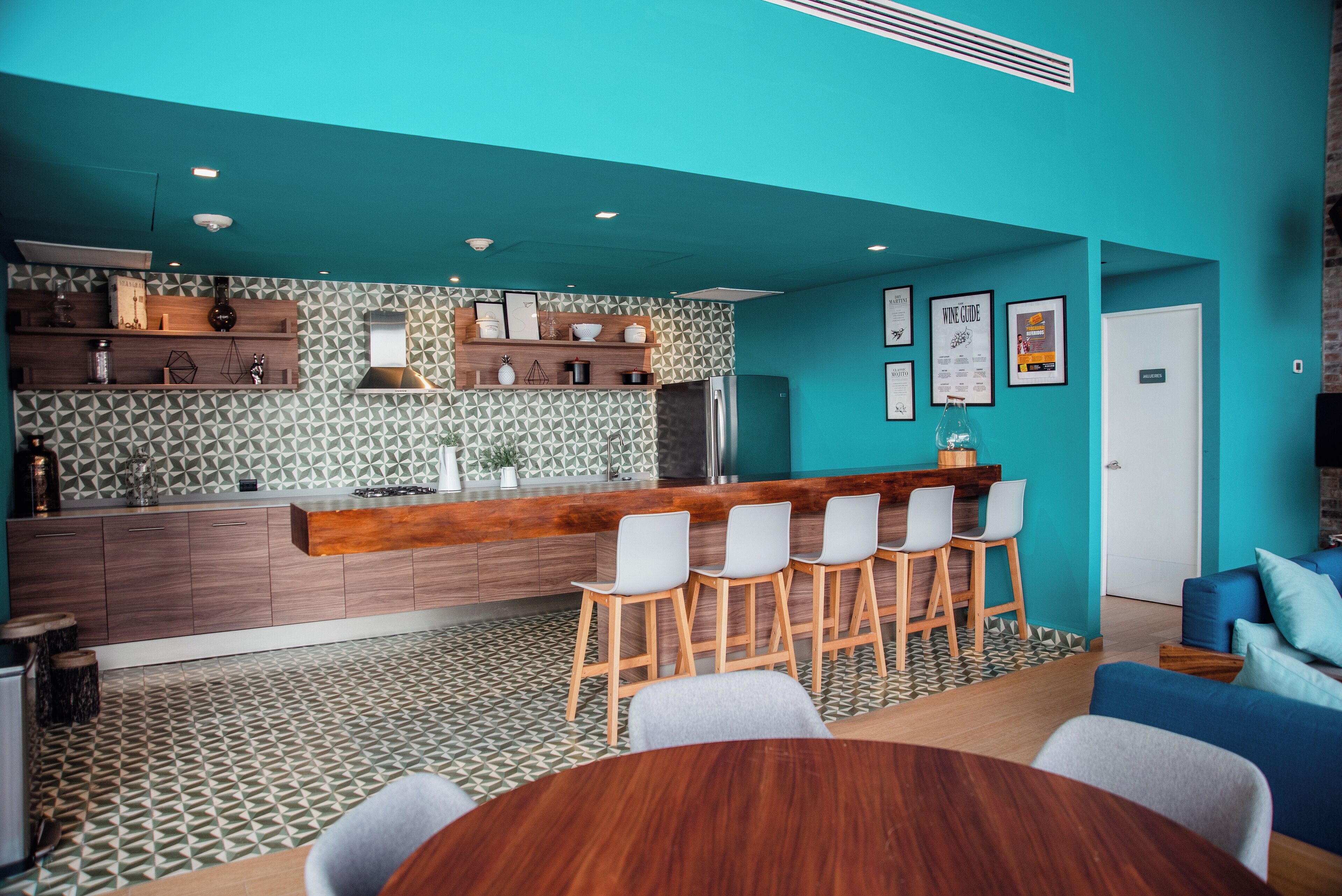 A modern kitchen with a bar area, wooden bar stools, and a dining table with chairs.