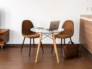 Een moderne kamer met een glazen tafel, twee leren stoelen, een laptop, een bruine lederen tas en een houten kast.