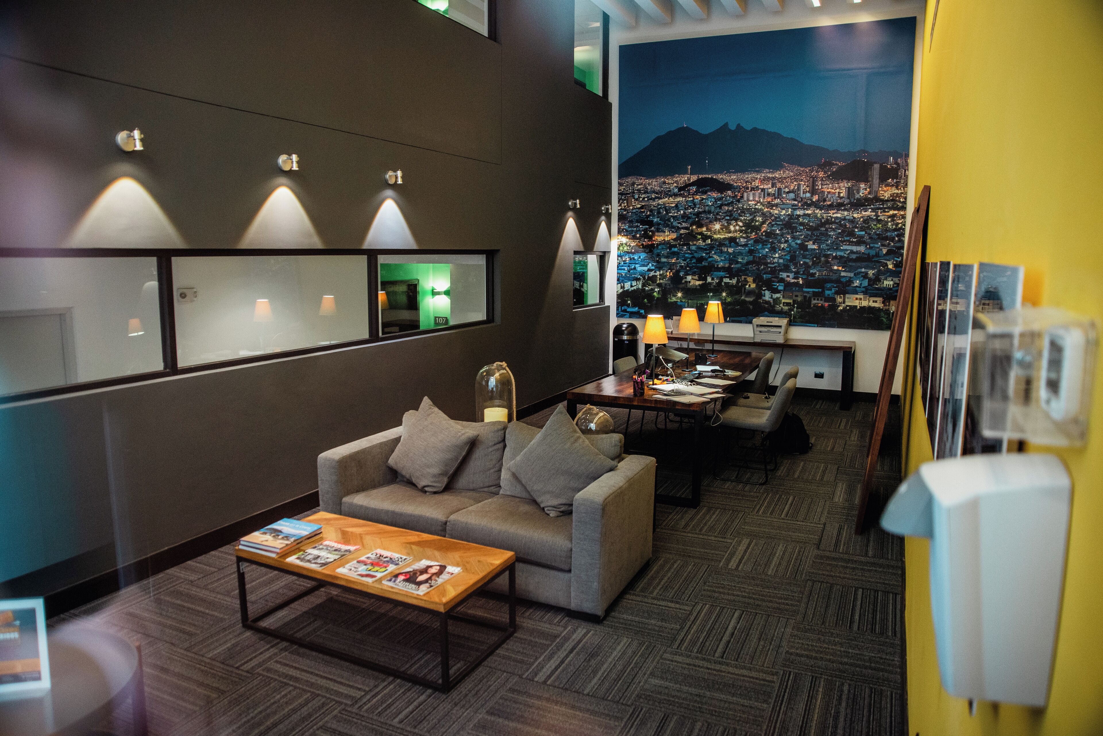 A modern hotel lobby with a sofa, coffee table, and a cityscape view through a large window.