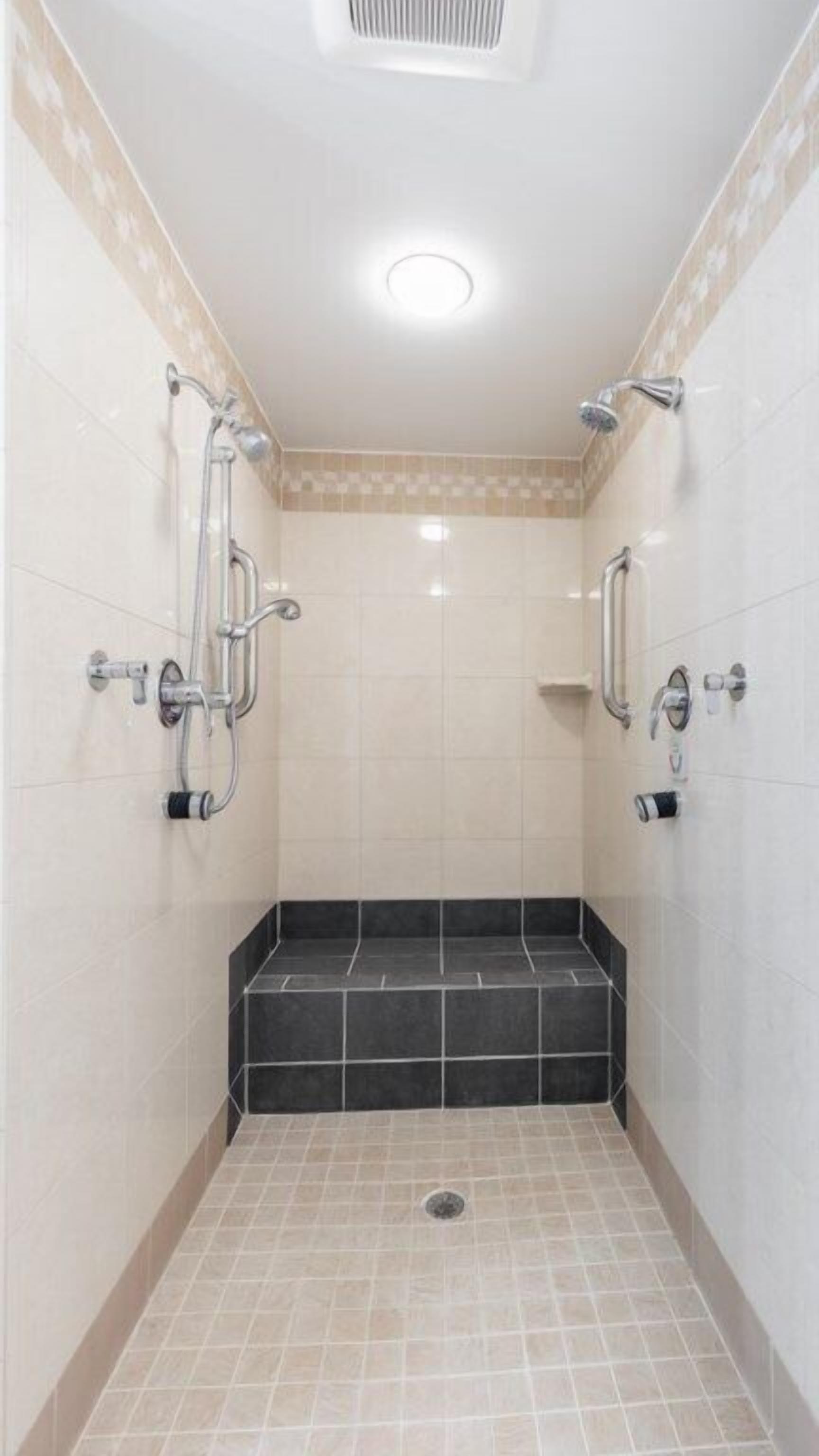 A small, tiled shower room with a black step and a ceiling light.