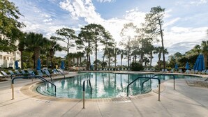 Un área de piscina con sillas de descanso y sombrillas, rodeada de árboles.