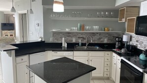 A modern kitchen with a black countertop, white cabinets, a built-in oven, and a hanging pendant light. - Wraparound Balcony provides Gorgeous Gulf Views from Every Room (Orange Beach)