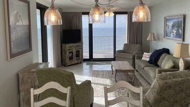 A living room with a view of the sea, a television, and a chandelier. - Wraparound Balcony provides Gorgeous Gulf Views from Every Room (Orange Beach)